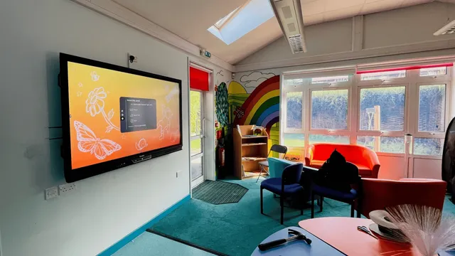 Primary school classroom with a wall-mounted interactive display beside a rainbow mural