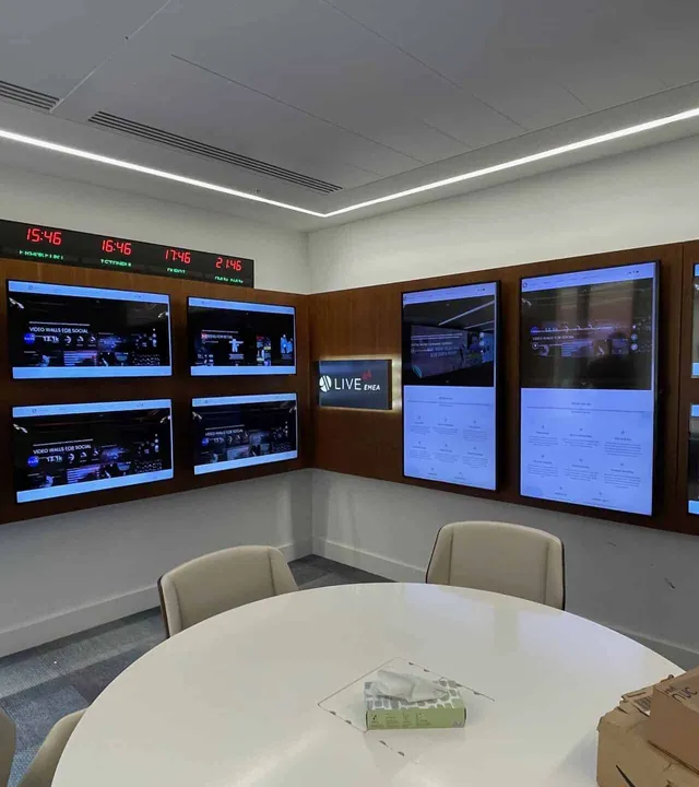 Meeting room lined with wall-mounted digital signage screens and a live ticker
